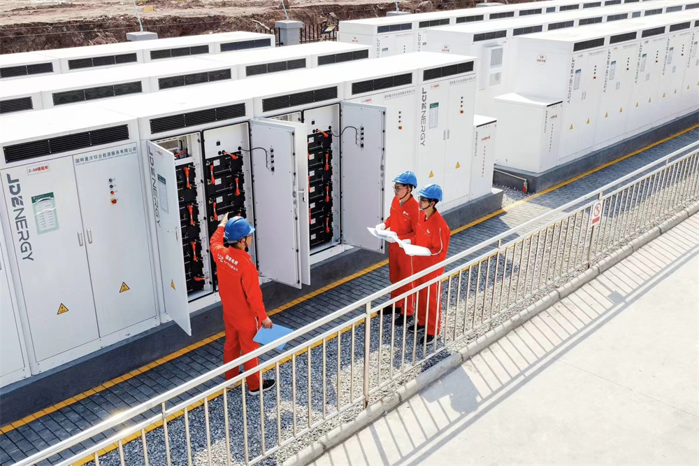 Workers inspecting an outdoor energy storage unit at a renewable energy facility.